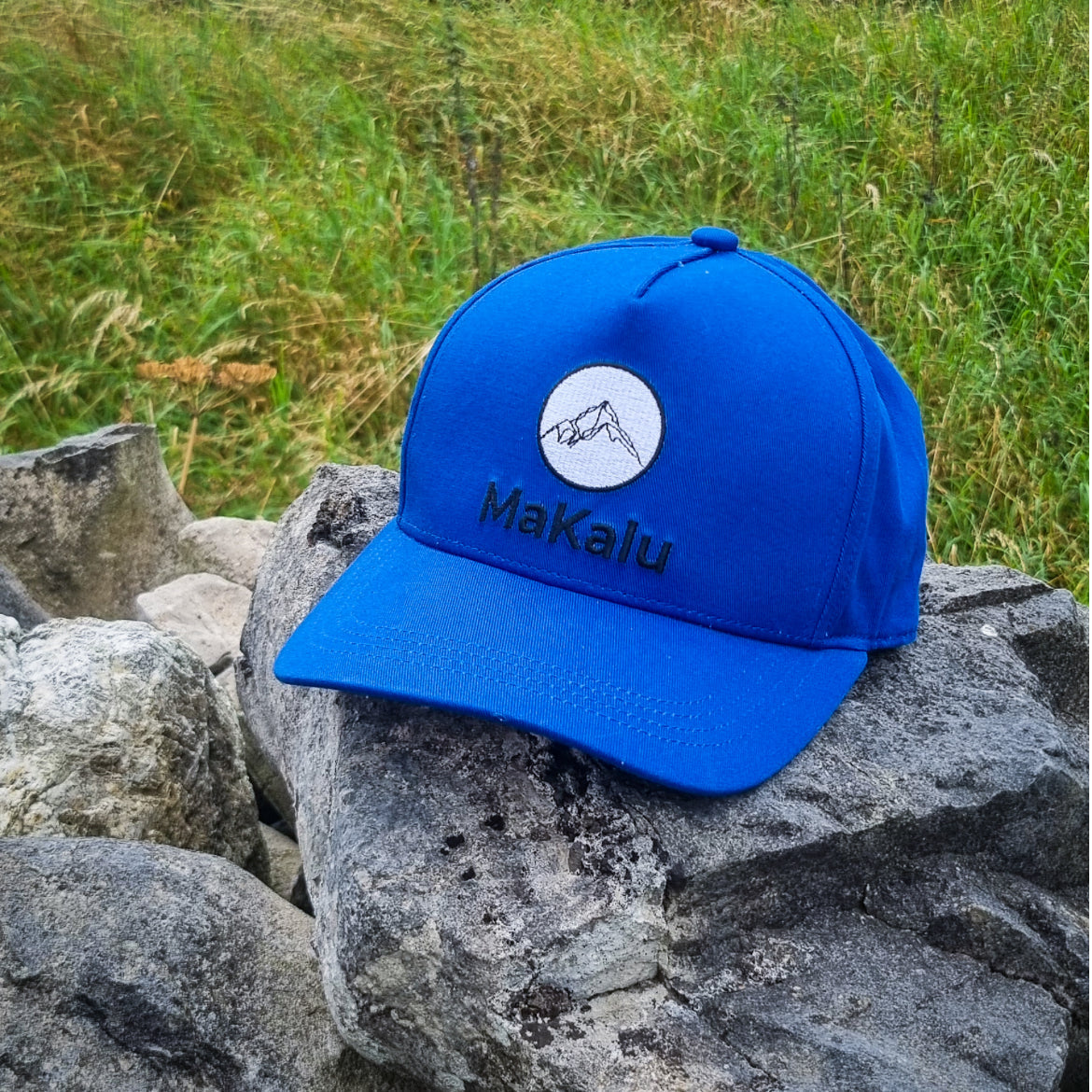 MaKalu blue designer cap with embroidered logo on rocks in outdoor setting